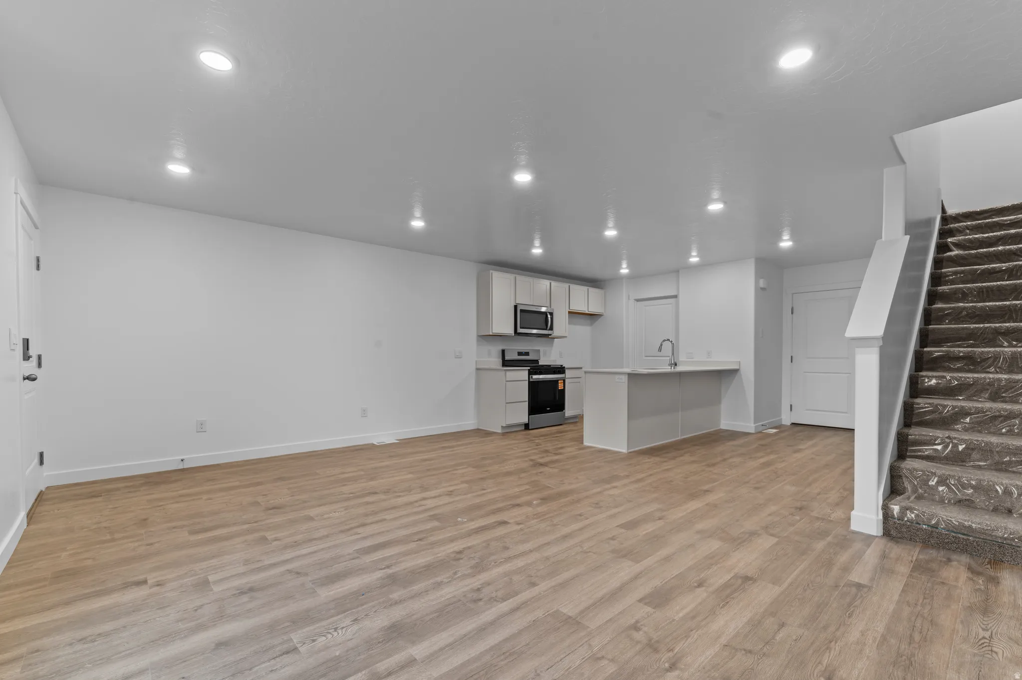 Kitchen with white cabinetry, light countertops, stainless steel appliances, open floor plan, and light wood-style flooring