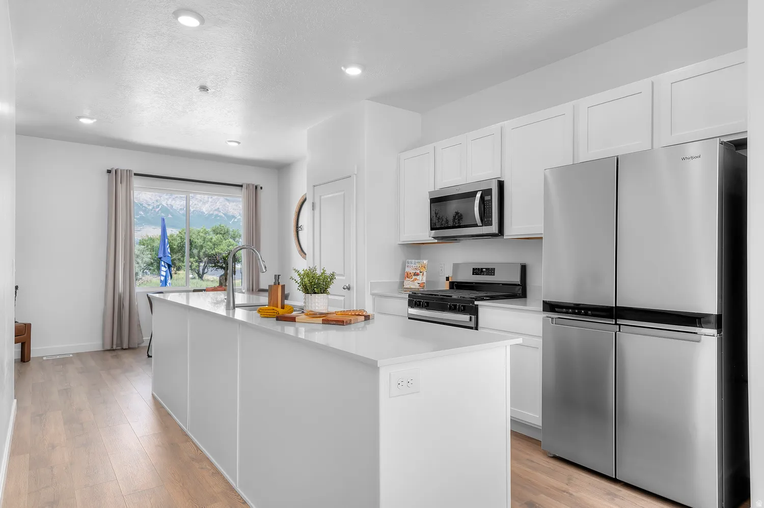 Kitchen with stainless steel appliances, white cabinetry, a kitchen island with sink, light wood finished floors, and light stone countertops