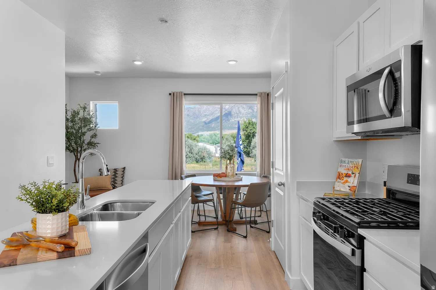 Kitchen with stainless steel appliances, white cabinetry, light wood-type flooring, and light stone counters