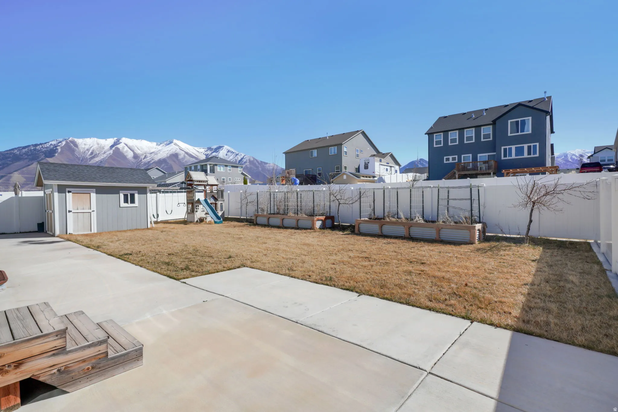 Fenced backyard featuring a residential view, a storage shed, a mountain view, a vegetable garden, and a patio