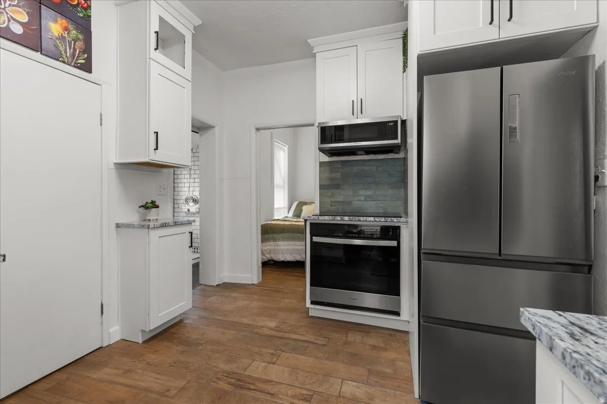 Kitchen with white cabinets, stainless steel appliances, light stone counters, dark wood-type flooring, and decorative backsplash