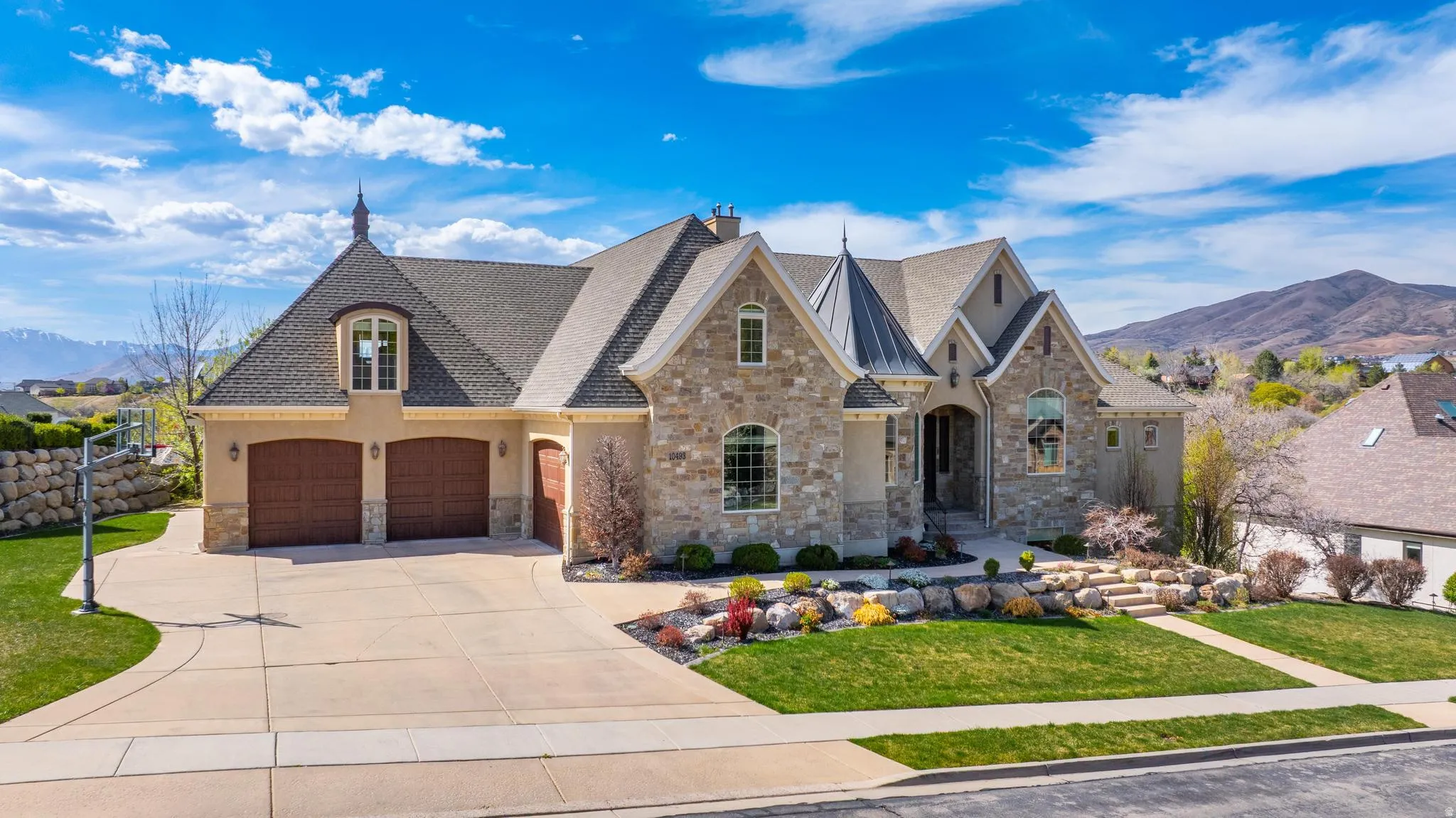 French country inspired facade featuring a mountain view, a front lawn, stone siding, and concrete driveway