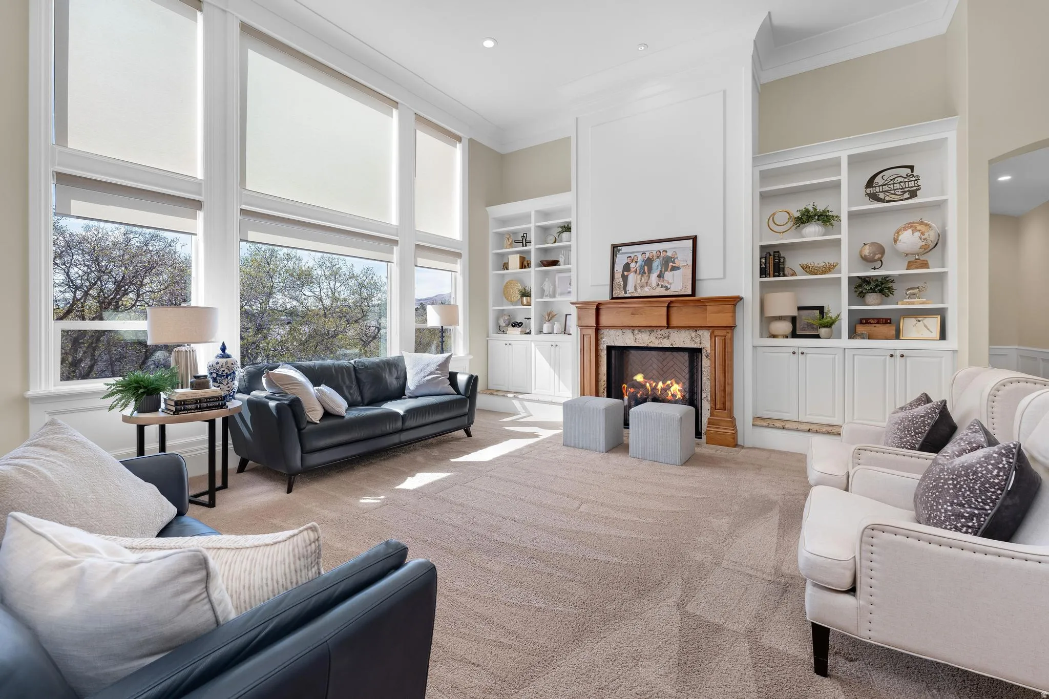 Living room featuring built in shelves, a high end fireplace, crown molding, carpet floors, and a high ceiling