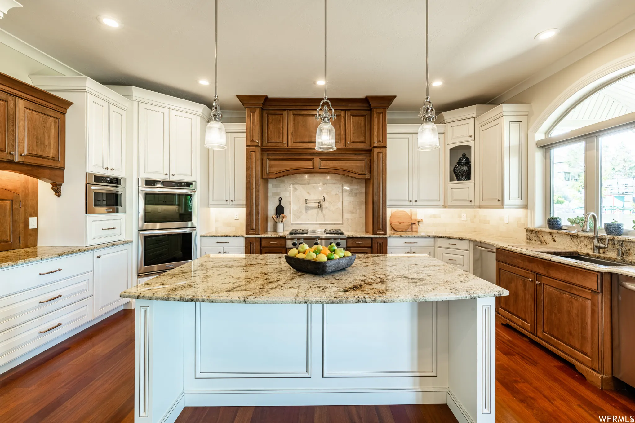 Kitchen featuring light stone countertops, backsplash, crown molding, a kitchen island, and decorative light fixtures