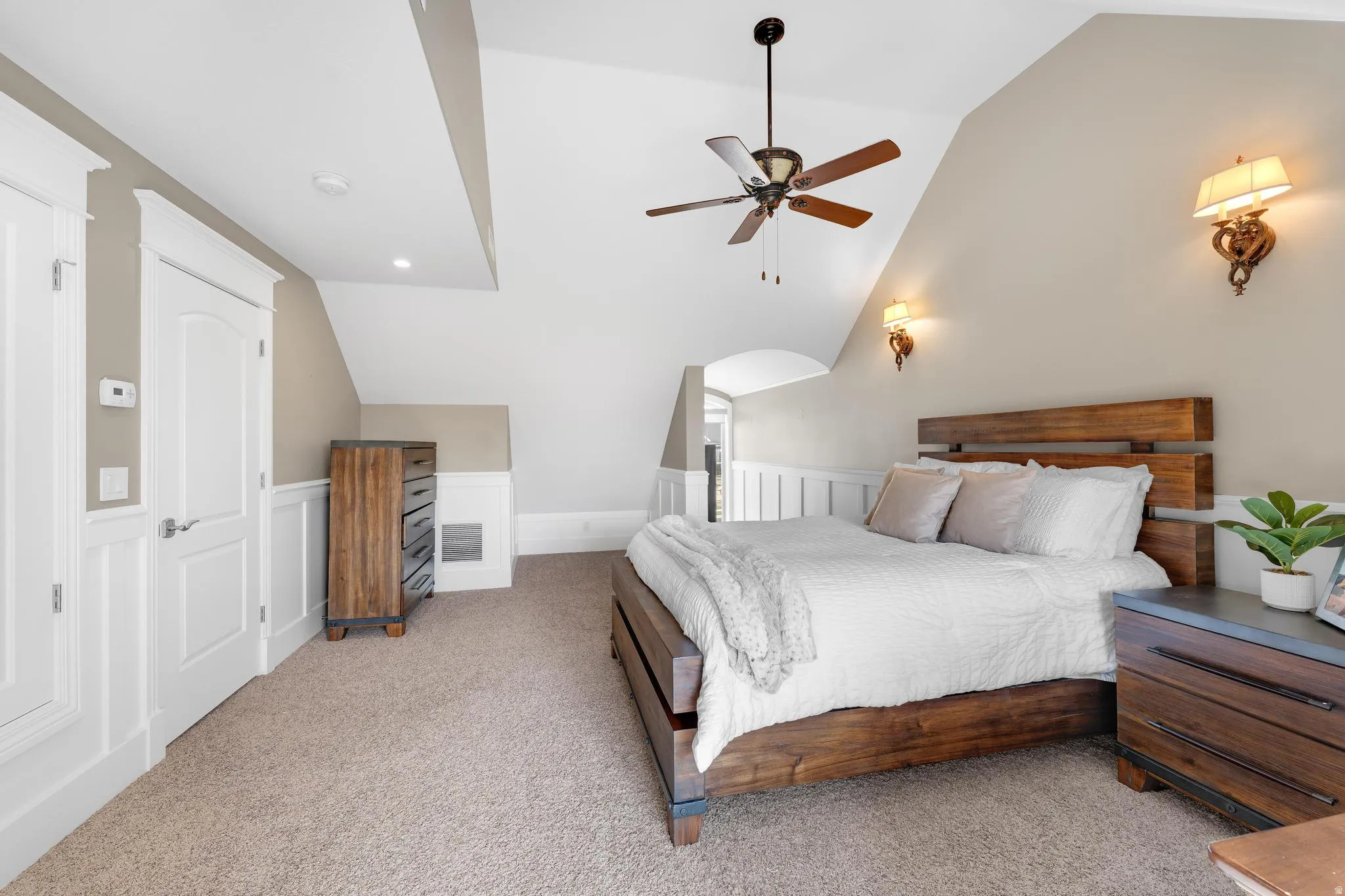 Carpeted bedroom with lofted ceiling, wainscoting, a decorative wall, and ceiling fan