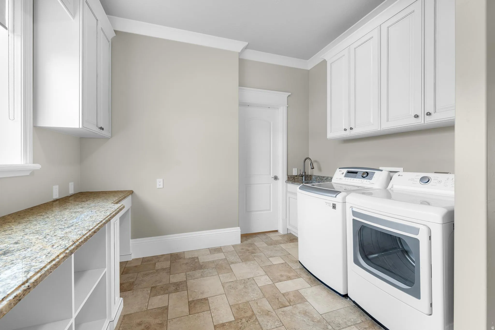 Laundry room with crown molding, washing machine and dryer, cabinet space, and stone finish floors