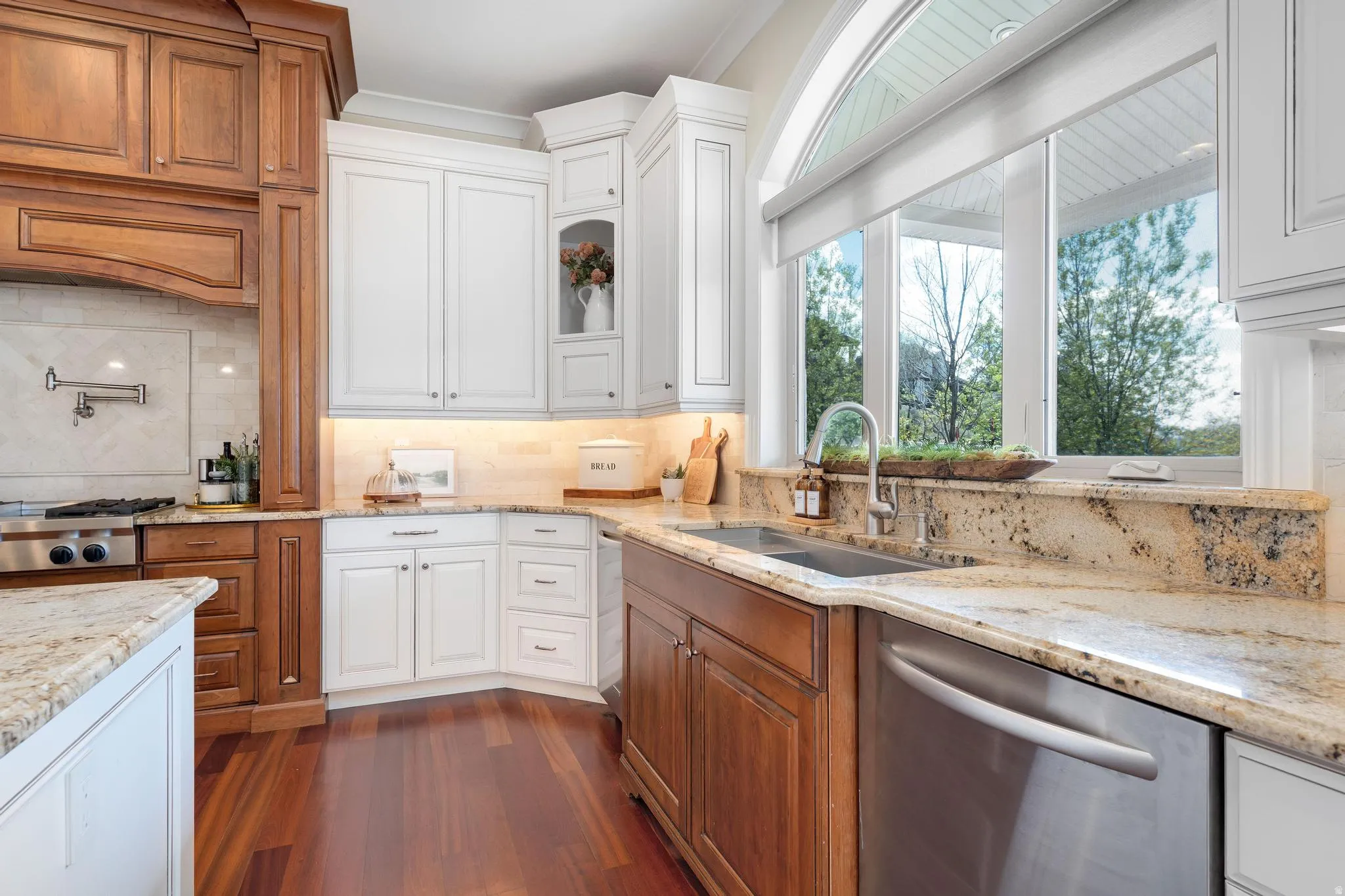 Kitchen featuring light stone counters, stainless steel dishwasher, tasteful backsplash, dark wood finished floors, and two tone cabinets