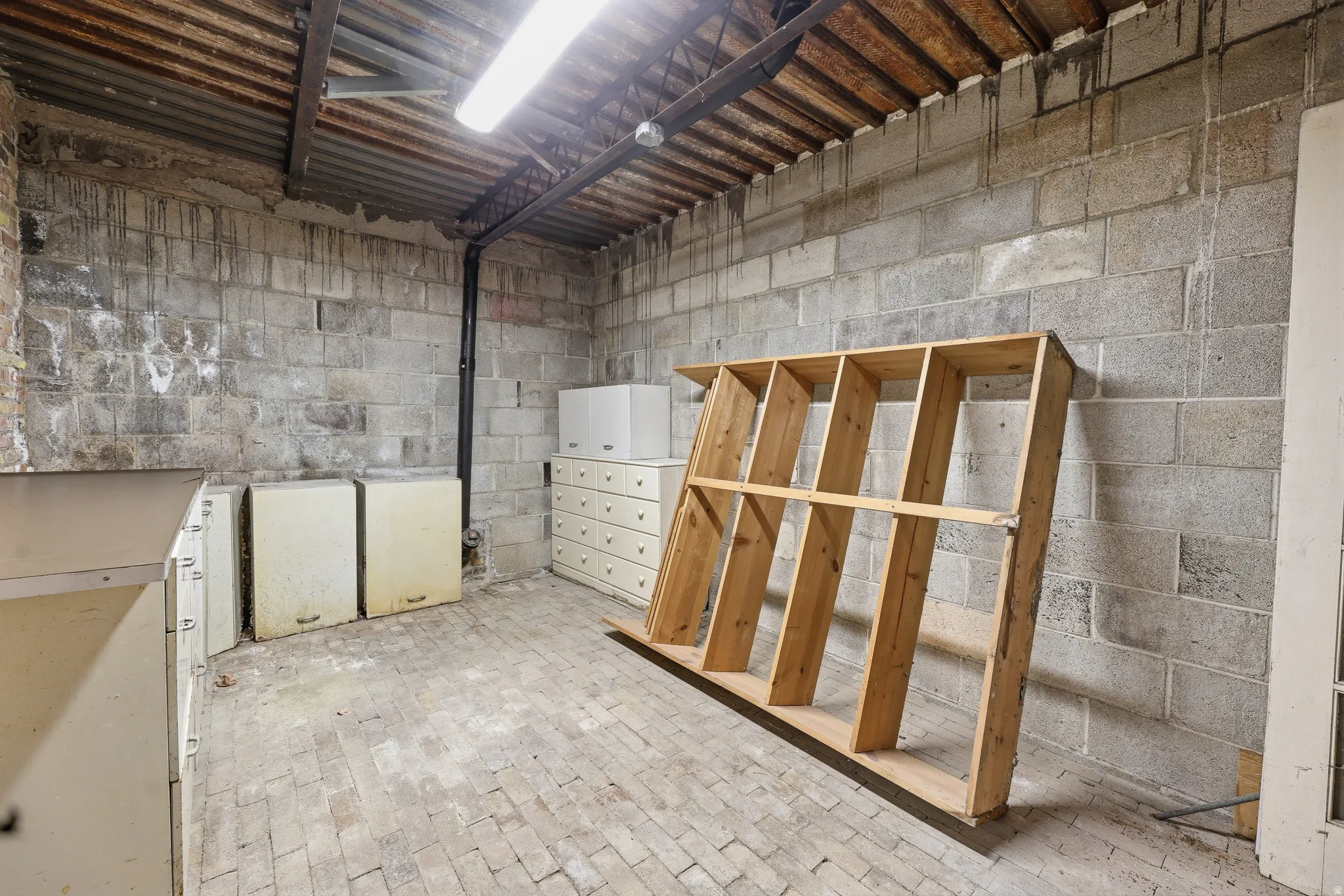Utility space featuring concrete block walls, brick paver flooring, and exposed corrugated metal ceiling