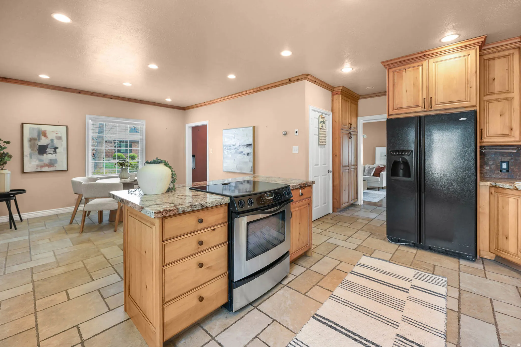 Kitchen with black refrigerator with ice dispenser, electric range, a kitchen island, recessed lighting, and stone tile flooring