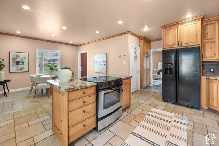 Kitchen with black refrigerator with ice dispenser, electric range, a kitchen island, recessed lighting, and stone tile flooring
