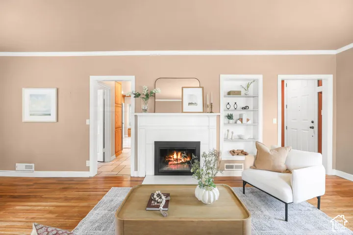 Living room with ornamental molding, light wood-type flooring, a fireplace with flush hearth, and built in features