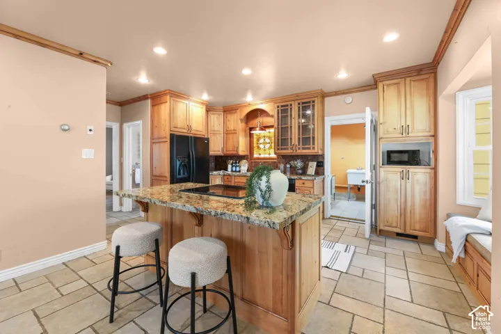 Kitchen featuring a kitchen breakfast bar, glass insert cabinets, black appliances, recessed lighting, and a center island