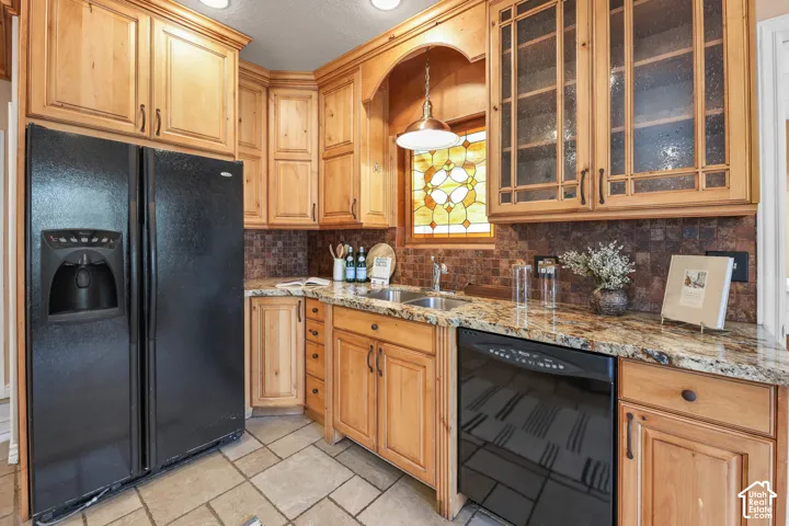 Kitchen featuring black appliances, glass fronted cabinets, light stone counters, decorative backsplash, and a textured ceiling