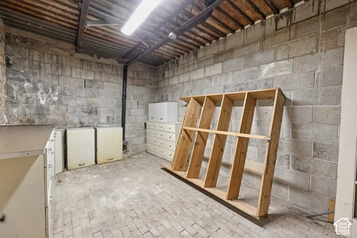 Utility space featuring concrete block walls, brick paver flooring, and exposed corrugated metal ceiling