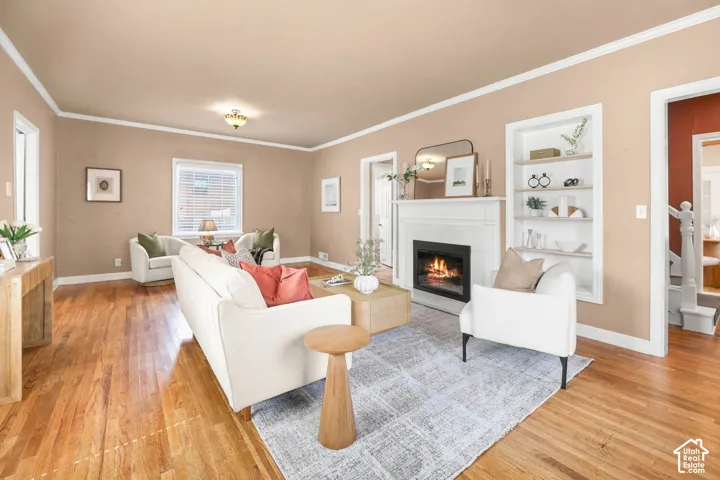 Living room with light wood-type flooring, a glass covered fireplace, ornamental molding, and built in features