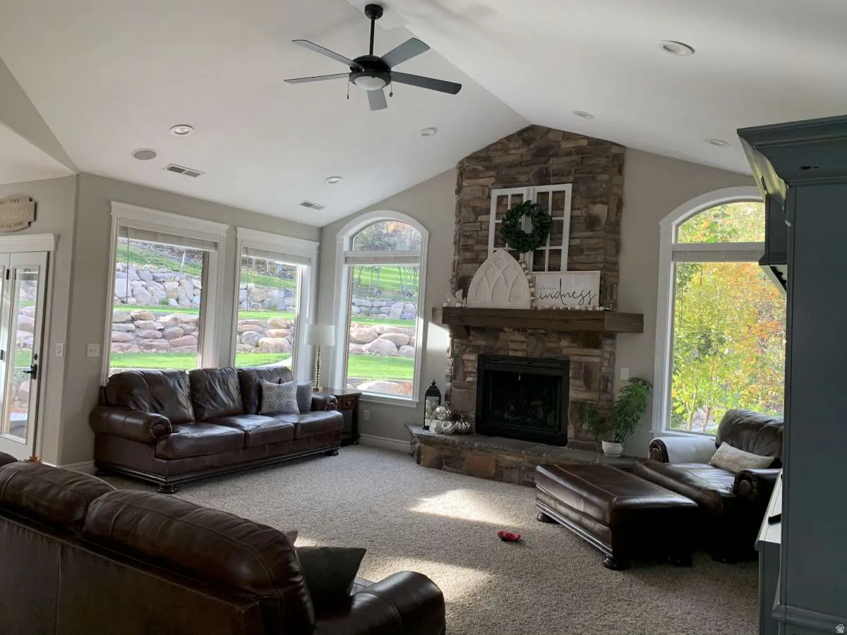 Living room with a ceiling fan, carpet flooring, plenty of natural light, and a stone fireplace