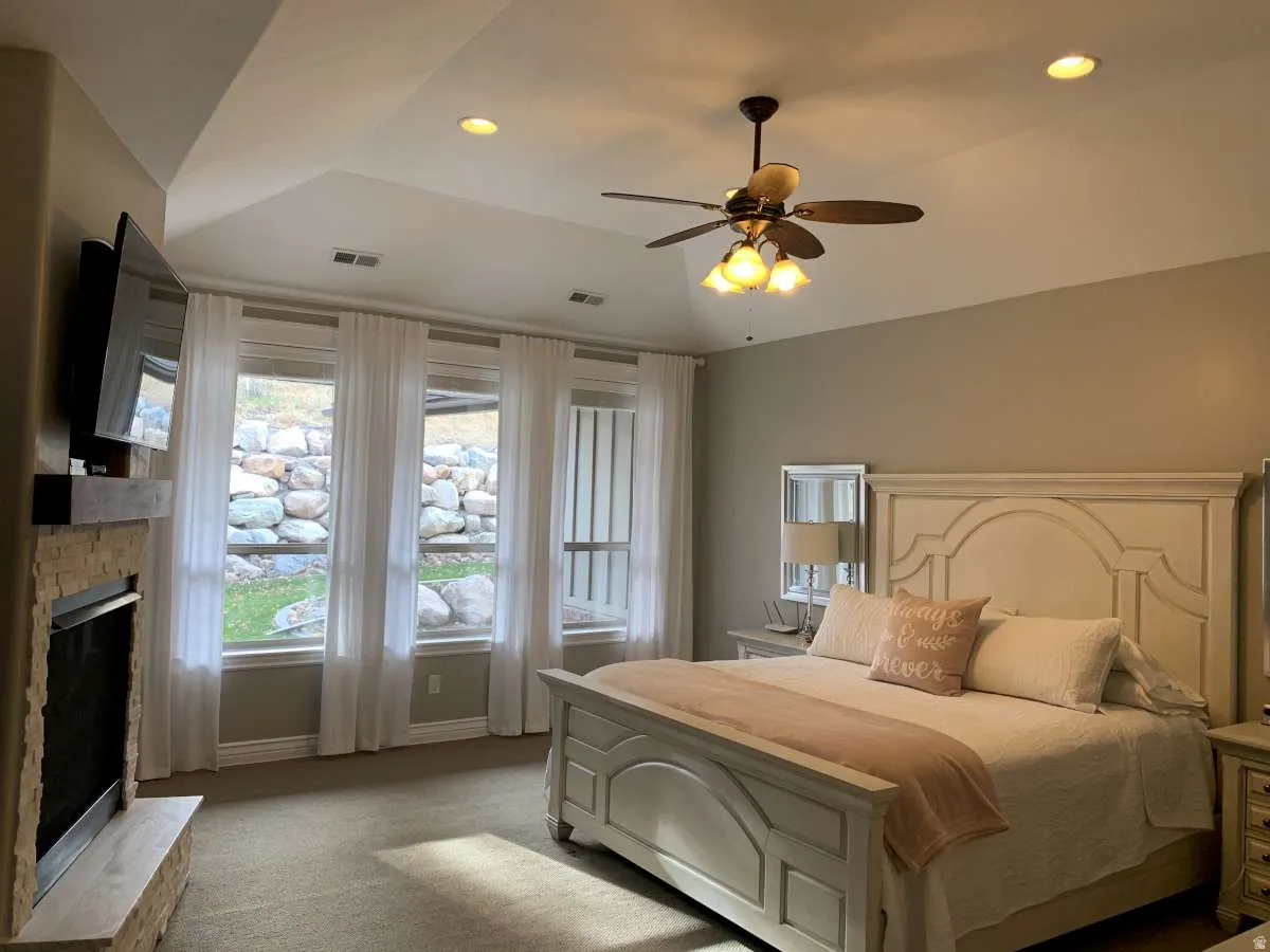 Bedroom with light colored carpet, recessed lighting, ceiling fan, lofted ceiling, and a fireplace with raised hearth
