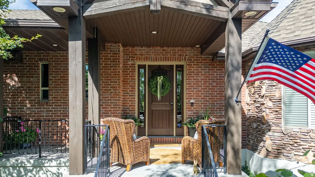 Brick facade entrance featuring a covered porch with exposed wood beams, a solid wood entry door with sidelights, and a stone accent wall