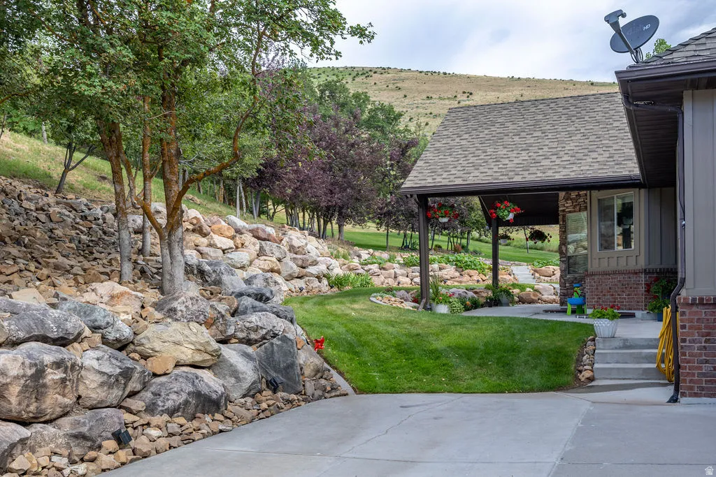 Exterior featuring a covered patio with a shingled roof, a concrete driveway, and a natural rock retaining wall