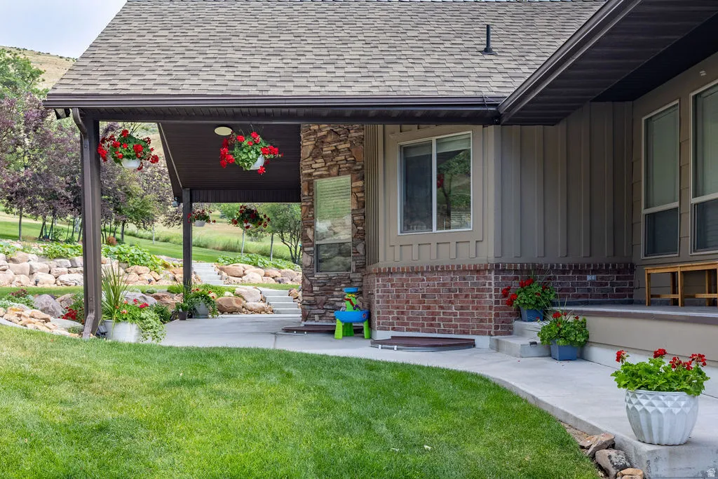 Exterior featuring a covered patio with stone pillar accents, a shingle roof, and a concrete pathway