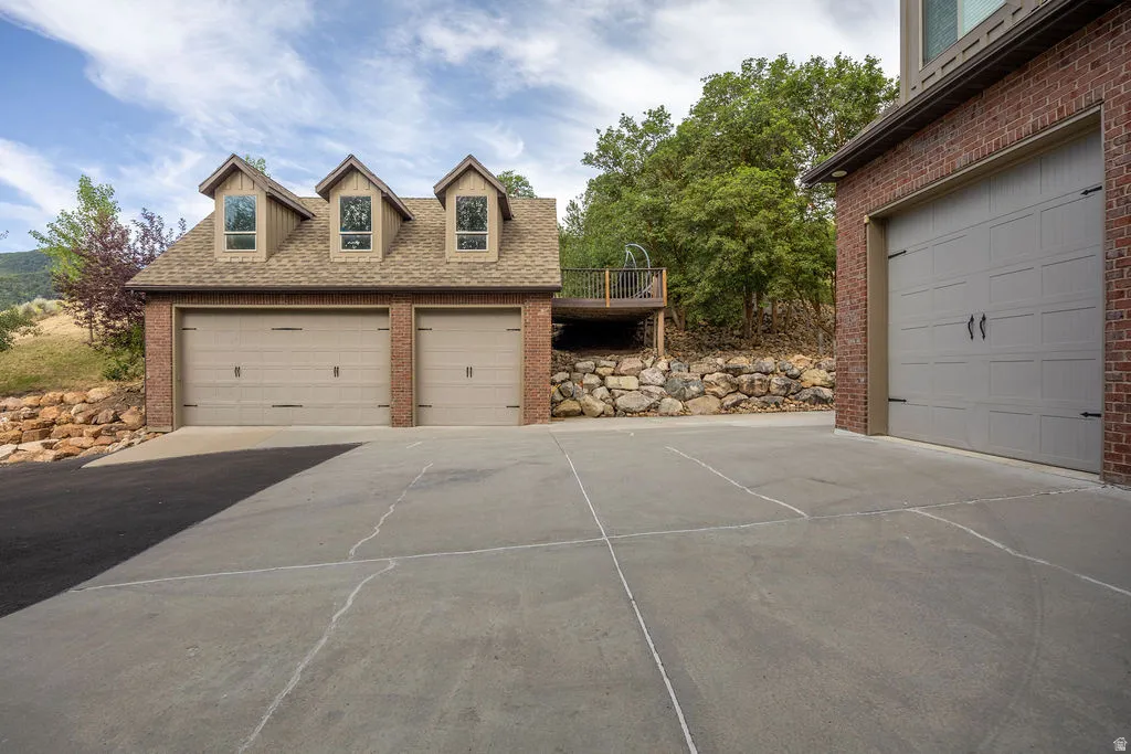 Extensive concrete driveway leading to a three-car garage structure with brick siding, dormer windows, and a shingle roof