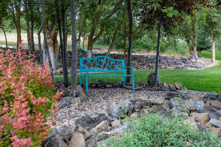 Landscaped exterior featuring natural stone borders, mature trees, manicured lawn, and a vibrant shrub