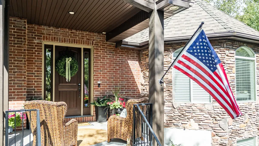 Brick and stone facade featuring an arched window, a covered porch with dark wood ceiling panels, and a prominent dark wood entry door with sidelights