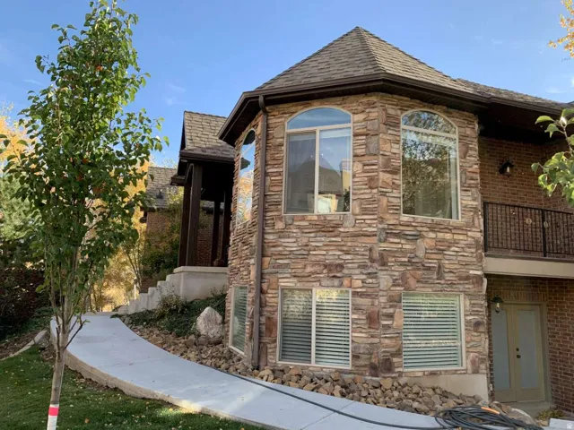 View of property exterior with roof with shingles, a balcony, and stone siding