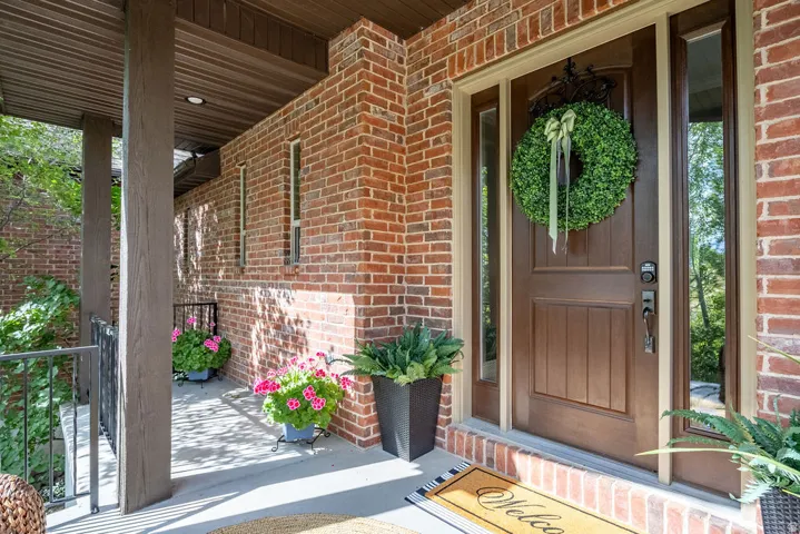 Brick facade entry featuring a paneled wood door with sidelights, a covered porch with a wood-finish ceiling, and structural columns