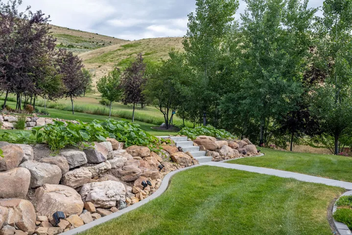 Landscaped yard featuring a stone retaining wall, concrete steps, and a curving pathway