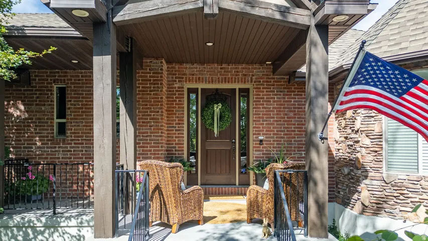 Brick facade entrance featuring a covered porch with exposed wood beams, a solid wood entry door with sidelights, and a stone accent wall