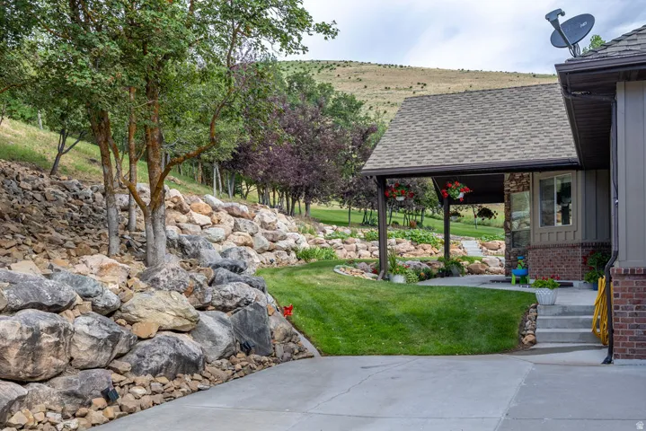 Exterior featuring a covered patio with a shingled roof, a concrete driveway, and a natural rock retaining wall