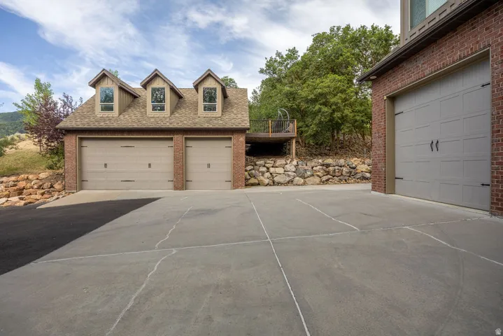 Extensive concrete driveway leading to a three-car garage structure with brick siding, dormer windows, and a shingle roof