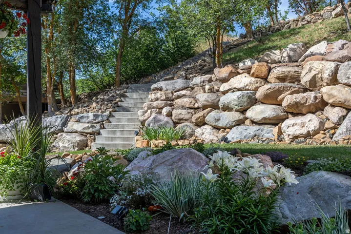 Terraced landscape featuring concrete steps, large natural stone retaining walls, mature trees, and diverse plantings