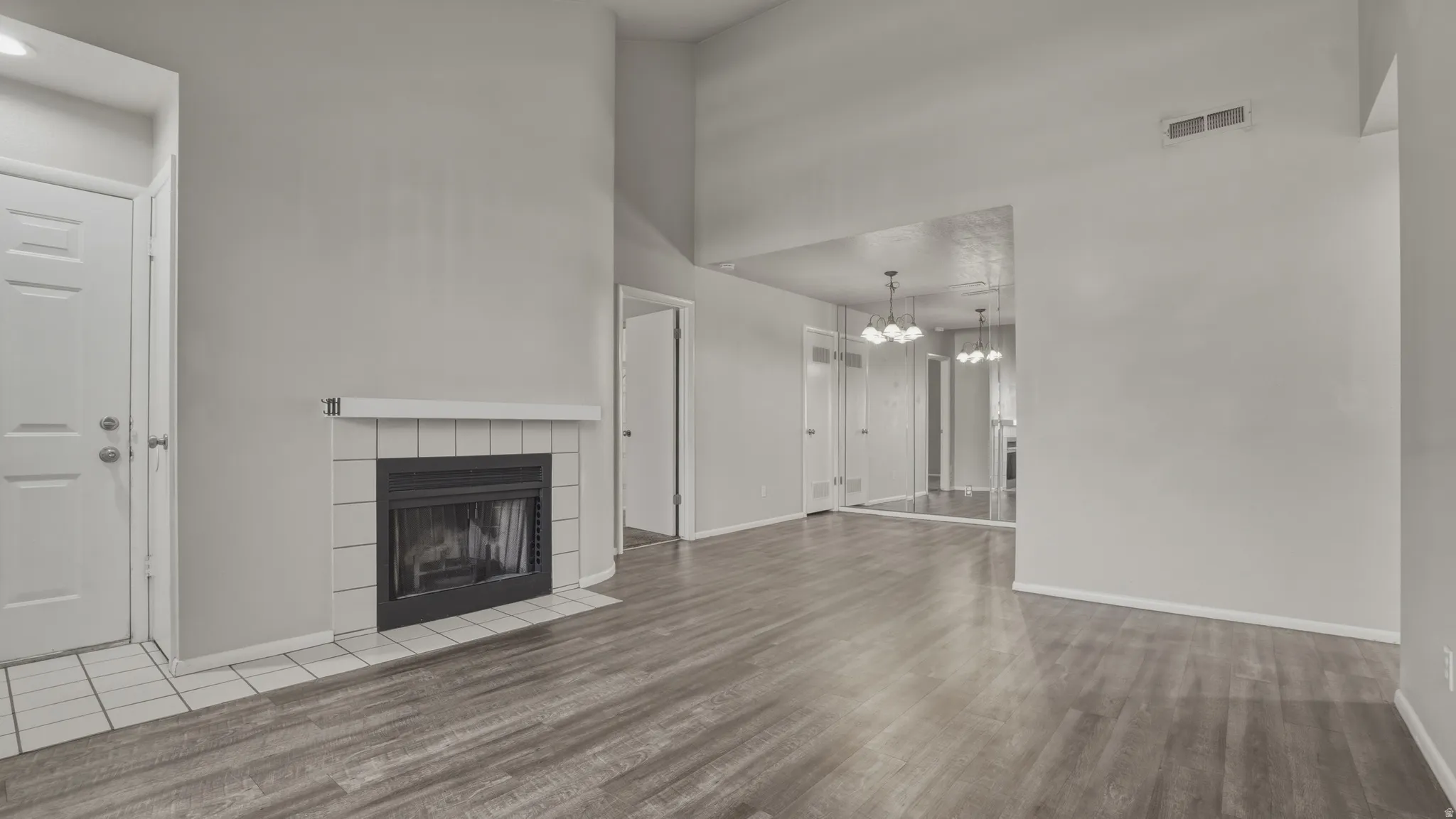 Unfurnished living room featuring a high ceiling, a tiled fireplace, hanging lights, and light wood finished floors