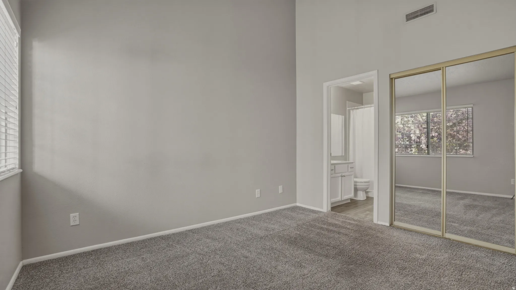 Unfurnished bedroom with carpet, a closet, ensuite bathroom, and a high ceiling