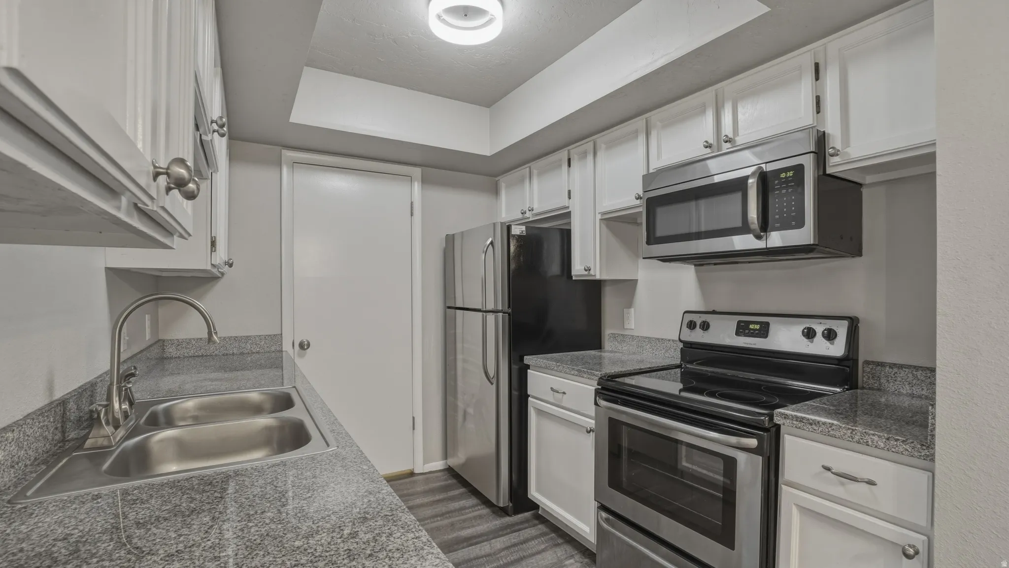 Kitchen with stainless steel appliances, white cabinetry, dark wood-type flooring, a tray ceiling, and dark countertops