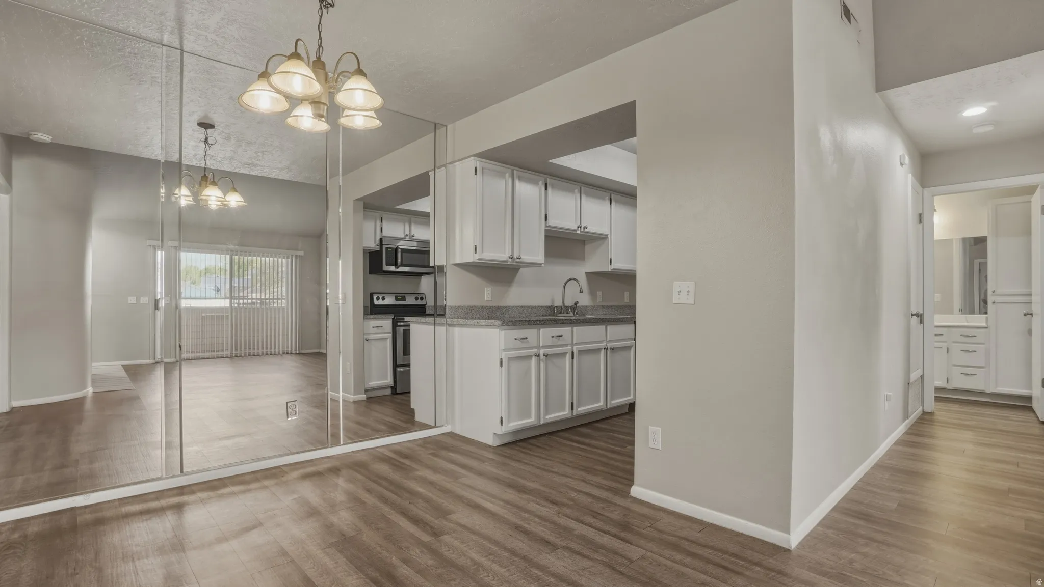 Kitchen with suspended lighting, white cabinetry, stainless steel appliances, and dark wood finished floors