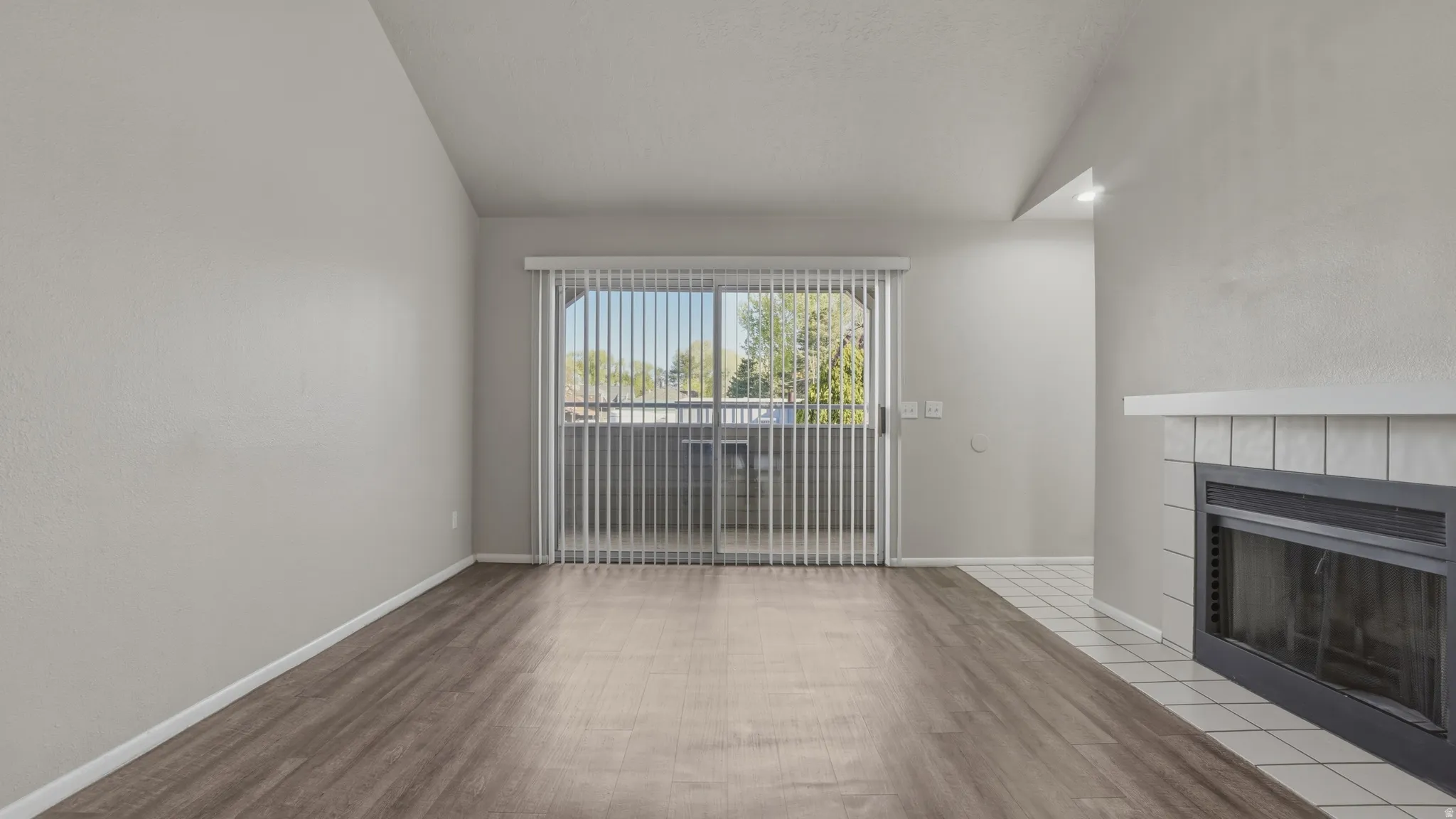 Unfurnished living room featuring a tiled fireplace, light wood finished floors, and lofted ceiling