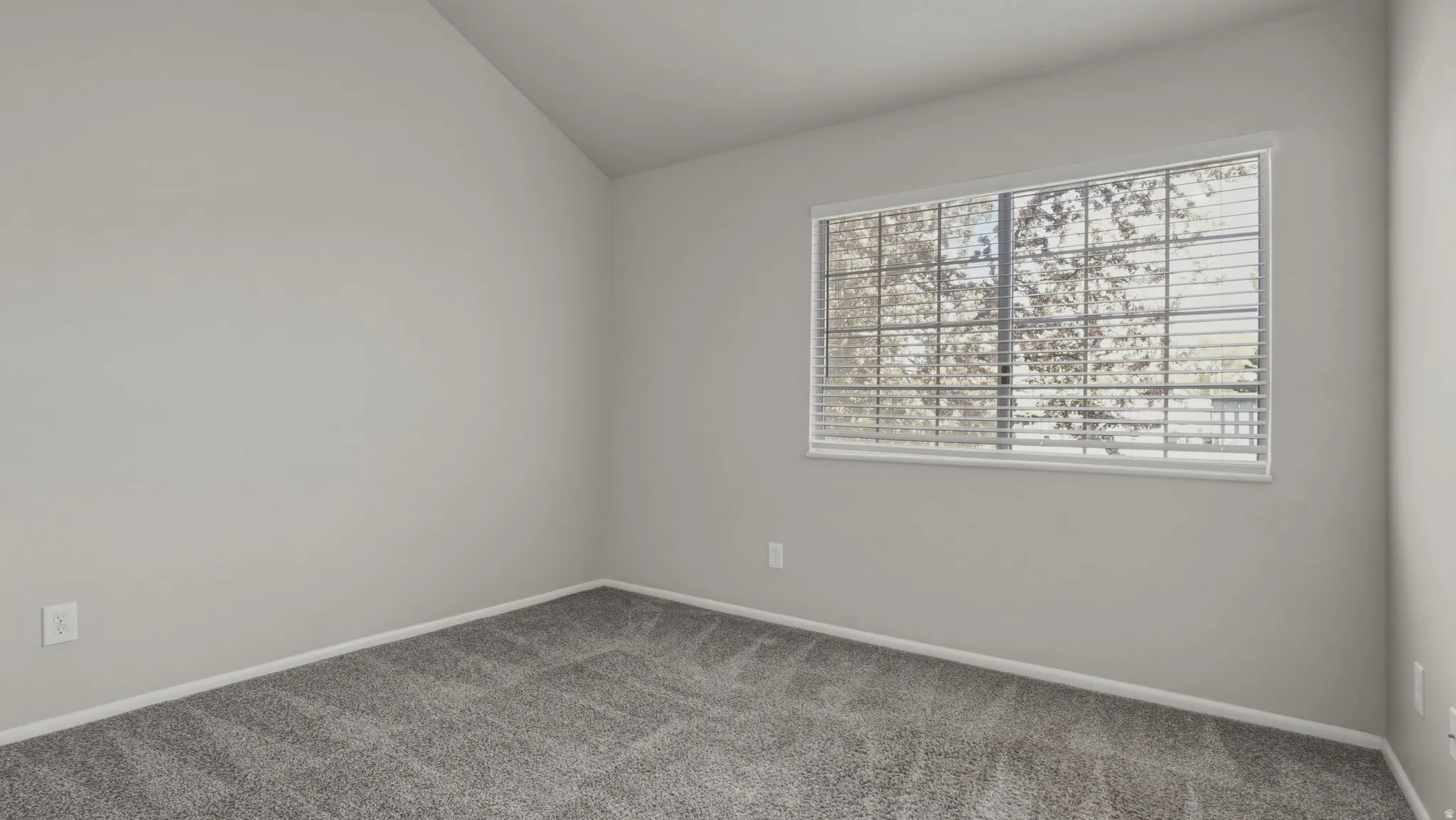 Carpeted empty room with lofted ceiling and baseboards