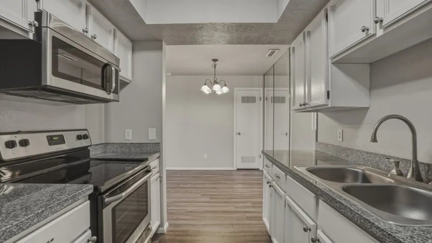 Kitchen with stainless steel appliances, dark countertops, white cabinets, and a chandelier