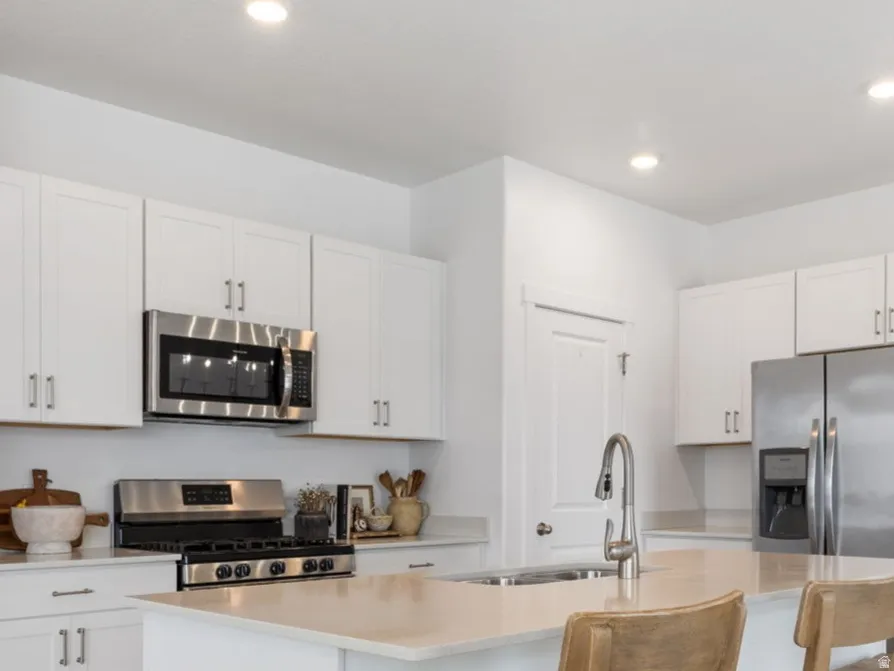 Kitchen featuring a kitchen bar, white cabinets, an island with sink, stainless steel appliances, and door to pantry