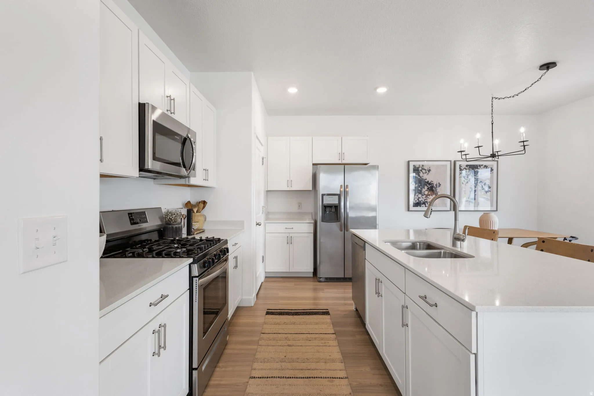 Kitchen featuring stainless steel appliances, an island with sink, white cabinetry, light wood-style floors and recessed lighting