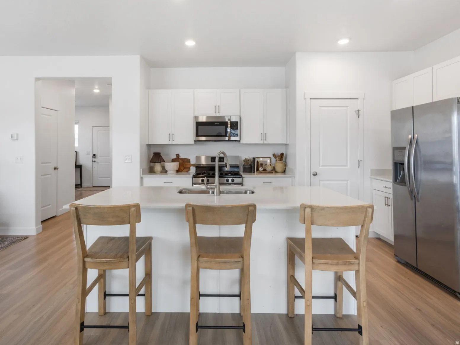 Kitchen with stainless steel appliances, white cabinets, light wood-style flooring, a center island with sink, and a breakfast bar