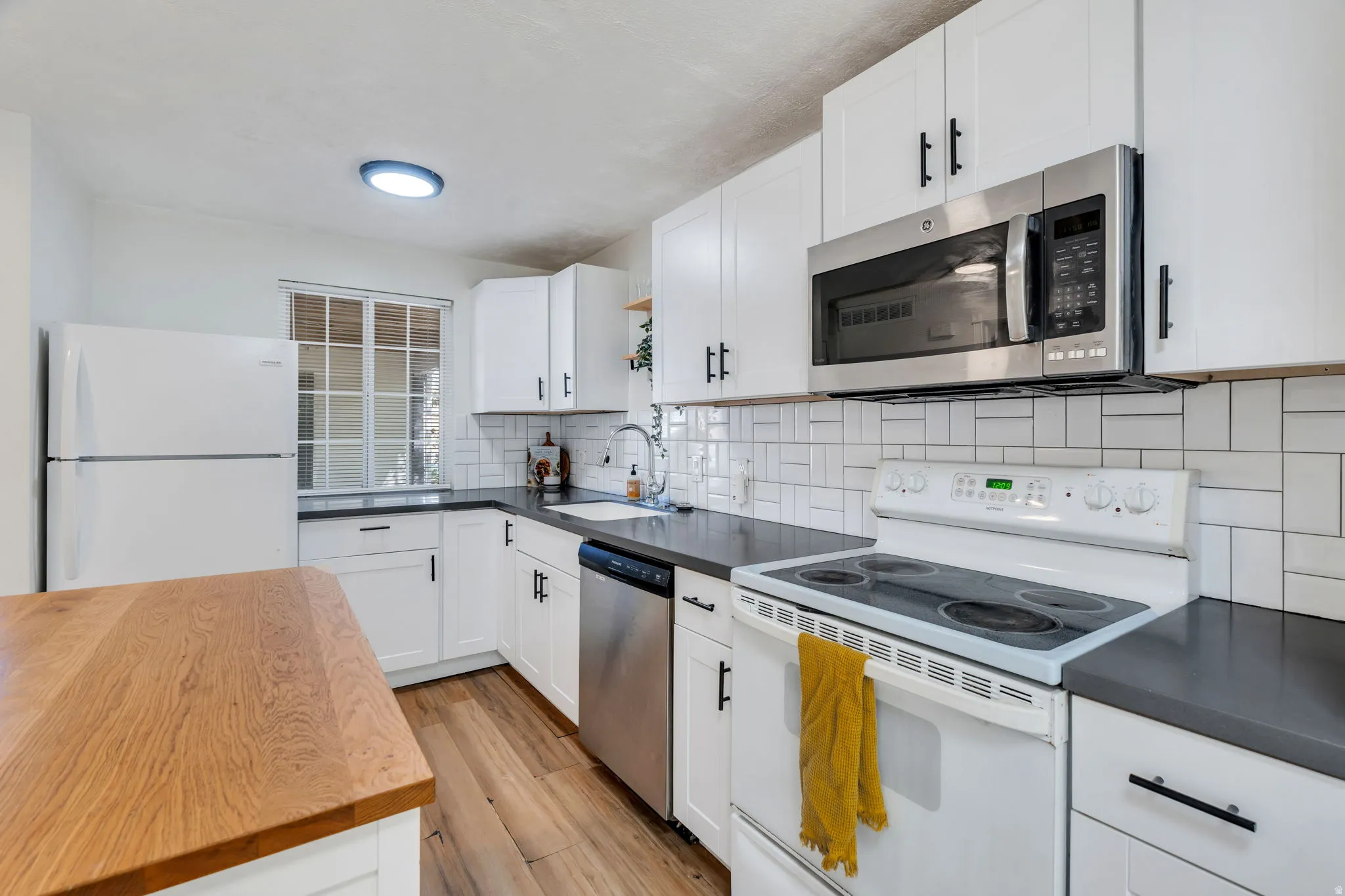 Kitchen with stainless steel appliances, white cabinetry, light wood finished floors, decorative backsplash, and open shelves