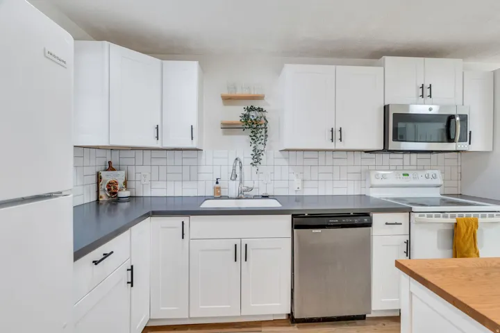 Kitchen with stainless steel appliances, white cabinets, open shelves, and backsplash