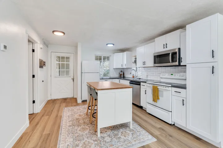 Kitchen with stainless steel appliances, decorative backsplash, white cabinetry, a center island, and light wood-style flooring