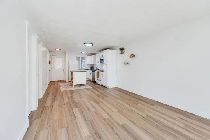 Kitchen with white cabinetry, light wood finished floors, a center island, white appliances, and decorative backsplash