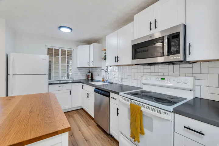 Kitchen with stainless steel appliances, white cabinetry, light wood finished floors, decorative backsplash, and open shelves