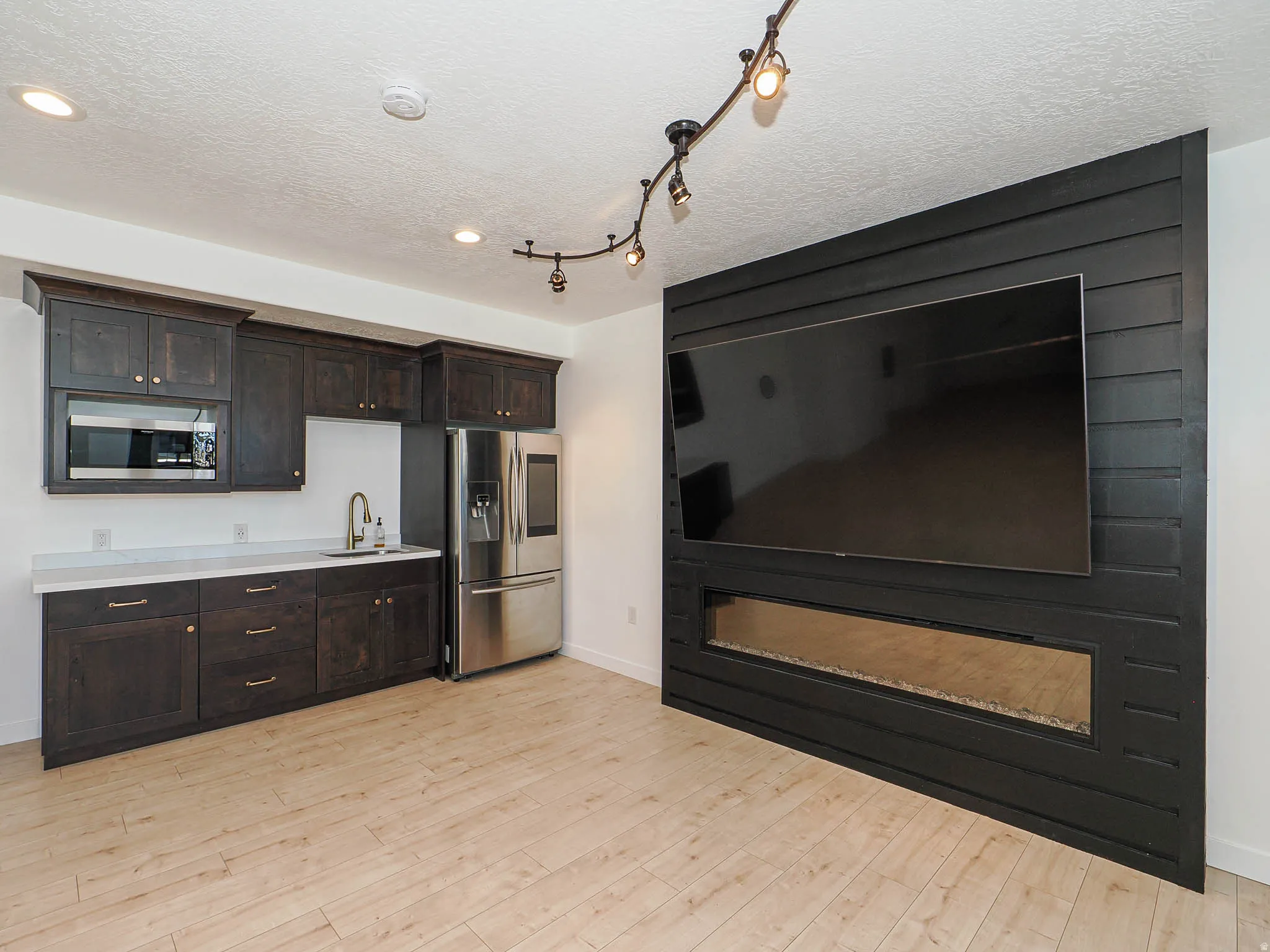 Kitchen with dark wood finish cabinets, light countertops, stainless steel appliances, light wood-style flooring, and a textured ceiling
